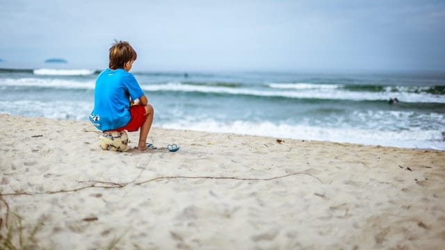 Kind sitzt alleine auf einem Ball am Strand