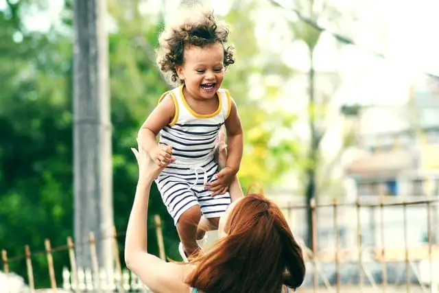 Frau hält Kind in die Luft, das lacht