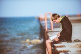 Kind sitzt auf einem Steg und hält die Beine in die Richtung des Wassers