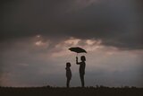 Ein Mensch hält den Regenschirm über sich und einen anderen Menschen