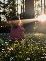 Kind draußen mit dem Rücken zur Kamera und Sonnenstrahlen im Gesicht 