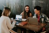 Drei Menschen sitzen mit Computer am Schreibtisch 