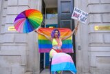 Mensch mit verschiedenen LGBTQ+ Flaggen und Schild "Born to be gay" in der Hand 